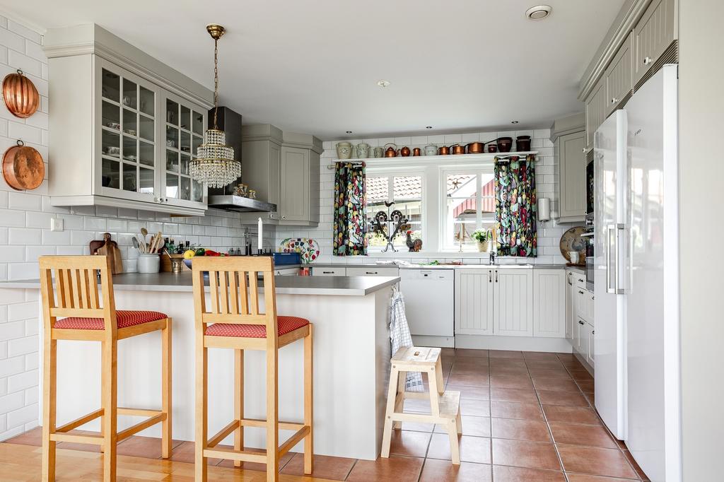Köksinredning från Marbodal i en varm grå/beige ton, kompletterad med grå laminatbänkskivor och vitt kakel som stänkskydd. 