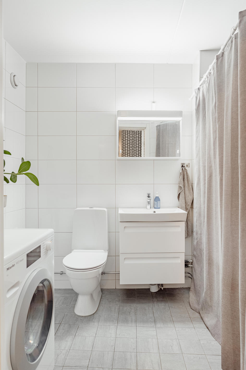 Fint helkaklat badrum utrustad med wc, handfat med kommod, badkar och tvättmaskin.