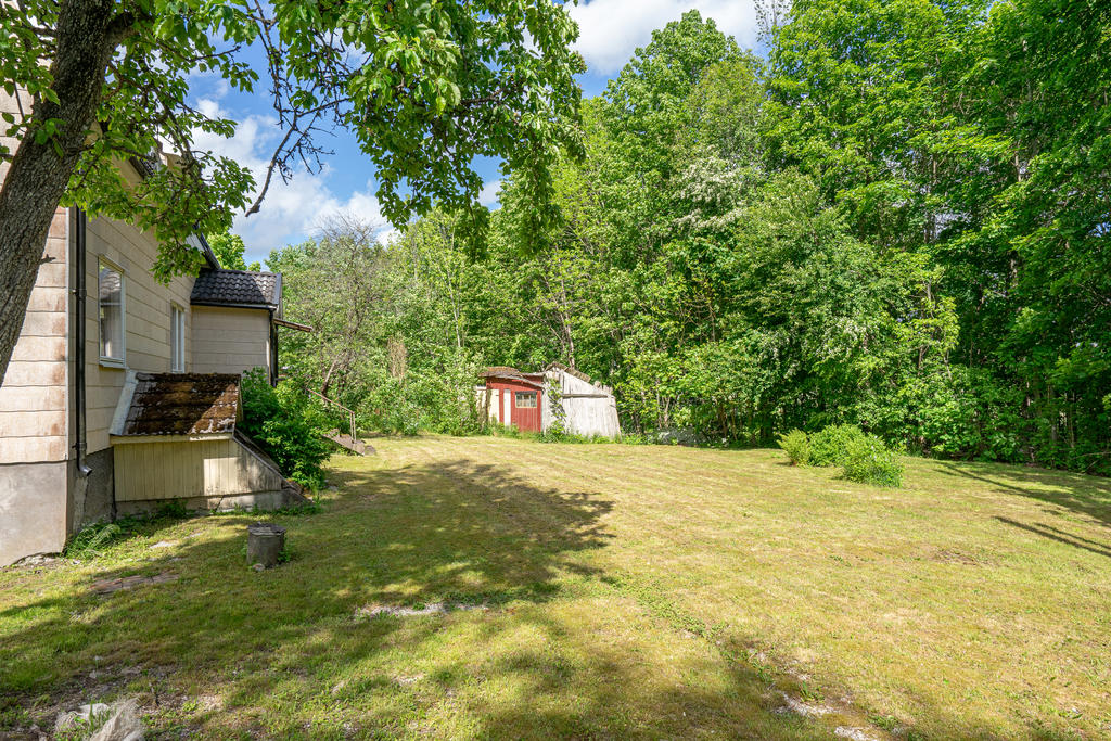 Rymlig trädgårdstomt med planteringar och äldre förrådsbyggnad.