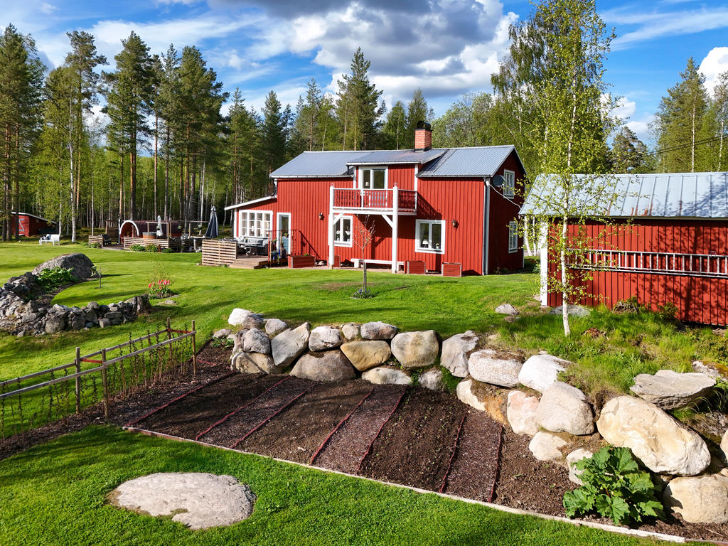 Fasad i sydväst med anlagd trädgård. På bild kan vi se hallonbuskar och grönsaksland. 