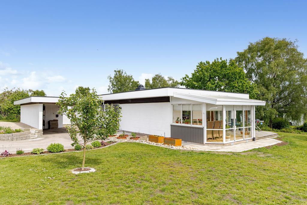 Huset omges av en plan trädgård med prydliga stendetaljer och upphöjda planteringsytor som bidrar till en strukturerad utemiljö