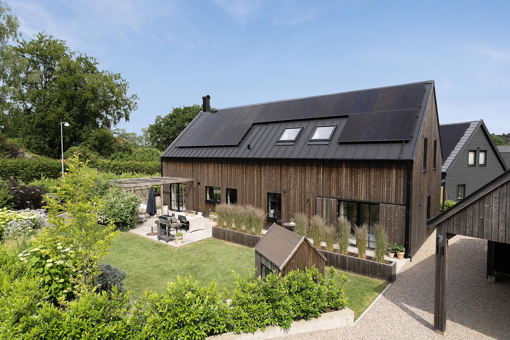Fasad med trädgård och uteplats framsida huset och parkering i prydlig carport. 