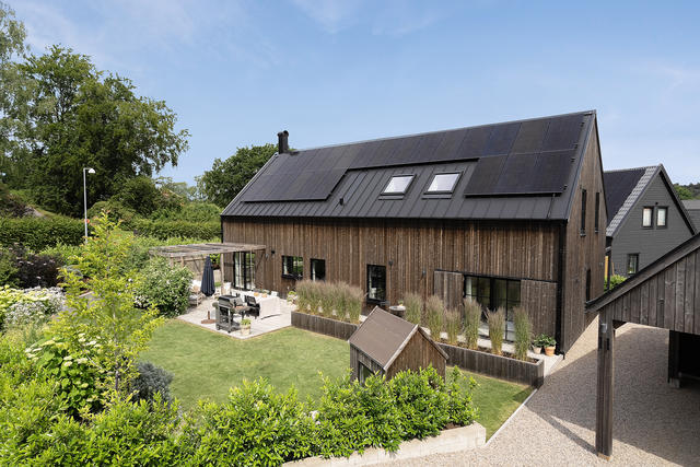 Fasad med trädgård och uteplats framsida huset och parkering i prydlig carport. 