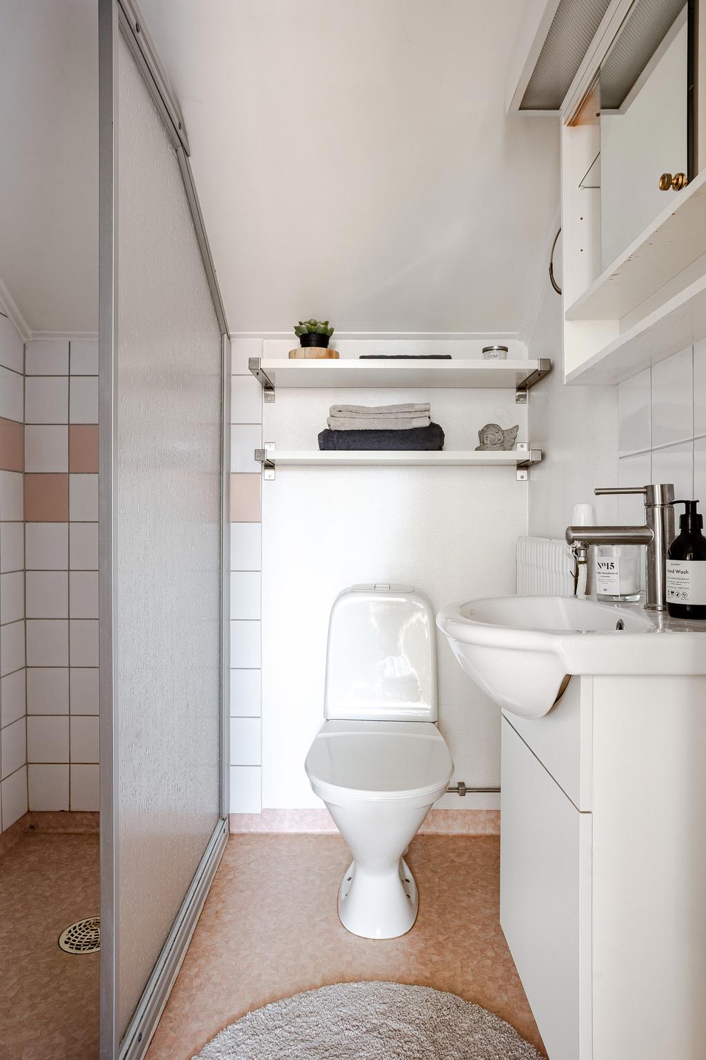 Badrum med dusch, WC, vitt kakel och våtrumsmatta