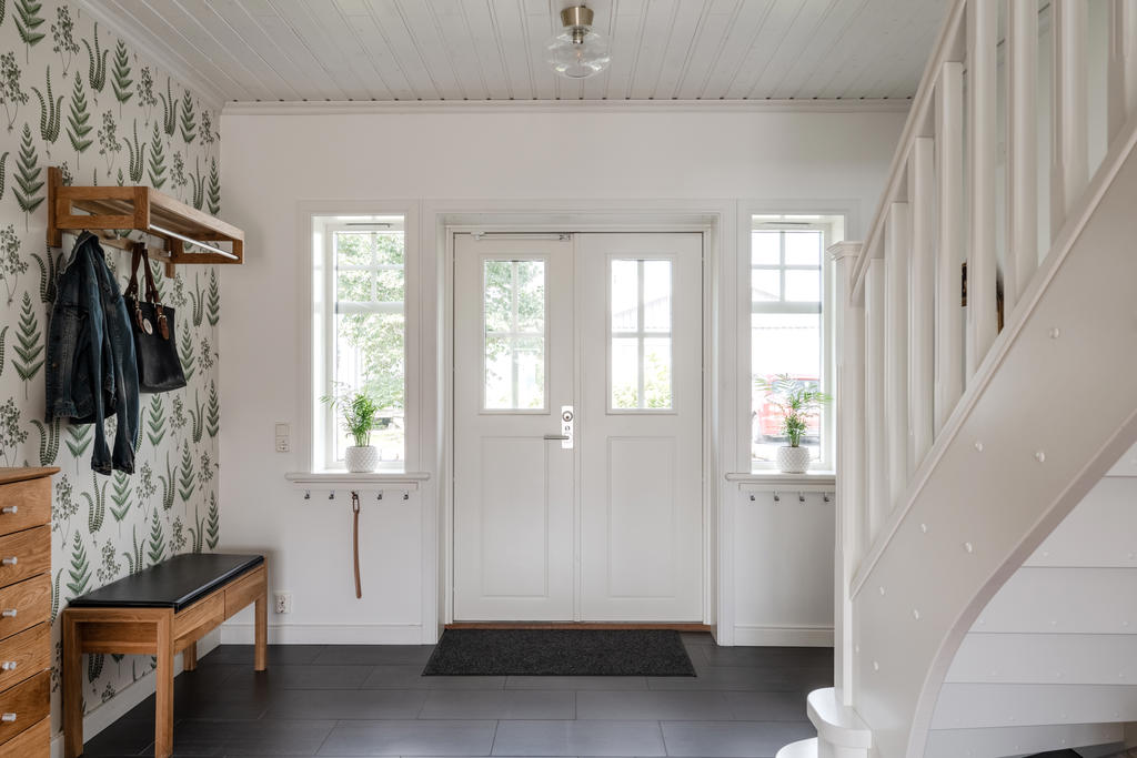 Via överbyggd entréveranda nås en stor och luftig hall. Möbleringsbar med gott om plats för skor och ytterkläder. Antracitgrått klinkergolv.