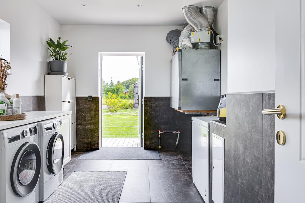 Tvättstugan är fullt utrustad med maskiner i arbetshöjd, generösa förvaringslösningar och praktiska bänkytor. En separat groventré gör utrymmet både funktionellt och lättillgängligt.