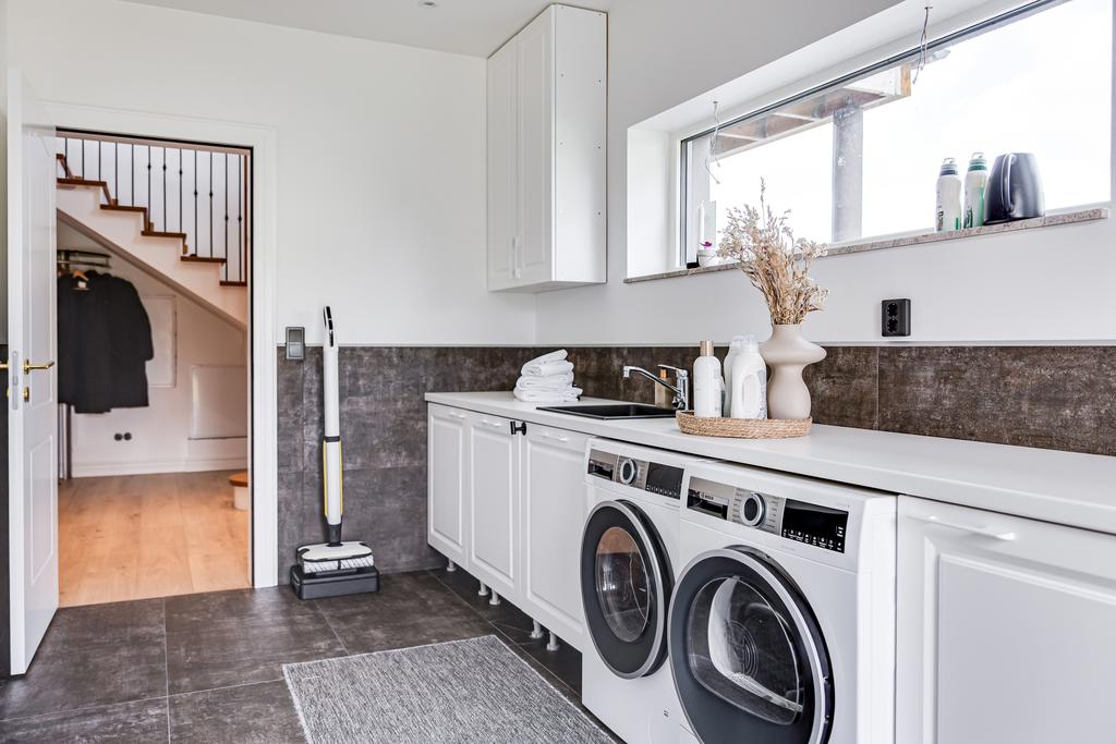 Modern tvättstuga med ljus stenskiva, underskåp, tvättmaskin och torktumlare. 