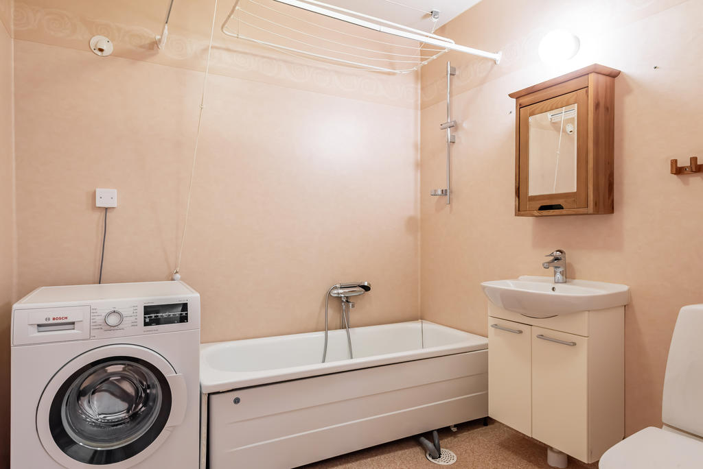 Badrum med tvättmaskin, wc, tvättställ med kommod, spegelskåp och badkar.