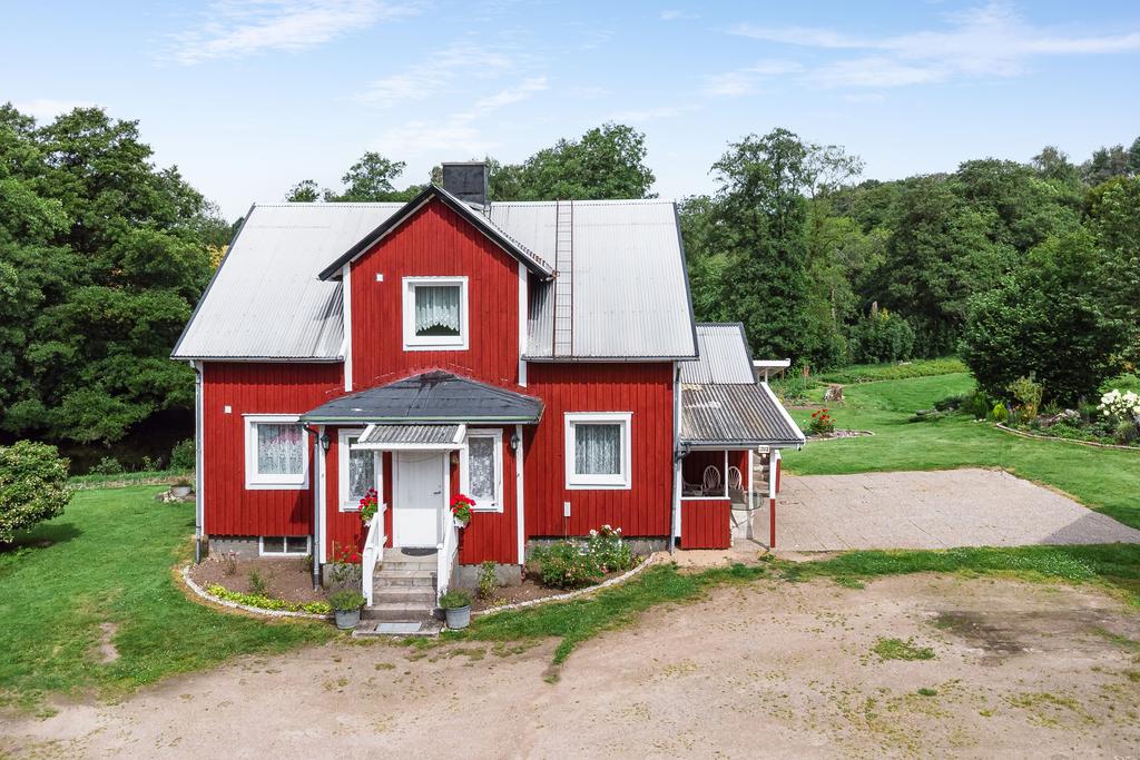 Ett charmig hus mitt i naturen, omgiven av grönskande träd och blå himmel.