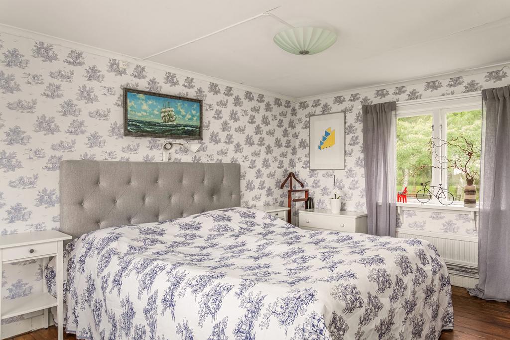 Master bedroom med mjuka toner, mönstrad fondvägg och fönster som ramar in den gröna omgivningen. Här finns det gått om plats för förvaringsmöbler. 