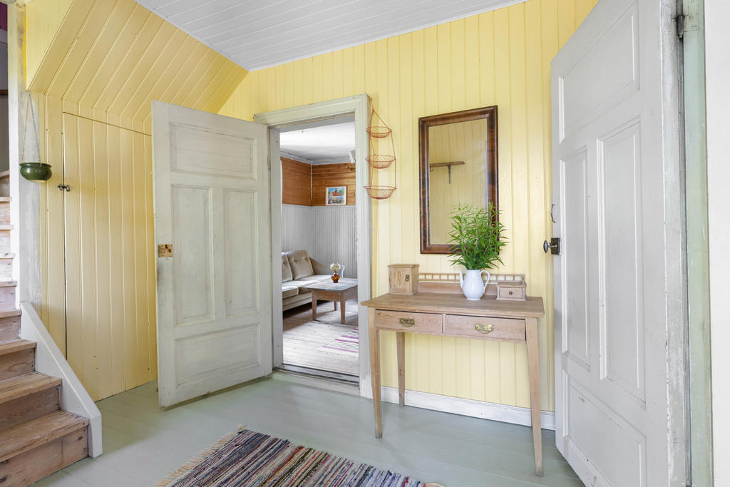 Hall med vy in till allrum och trätrapp upp till övervåningen. 