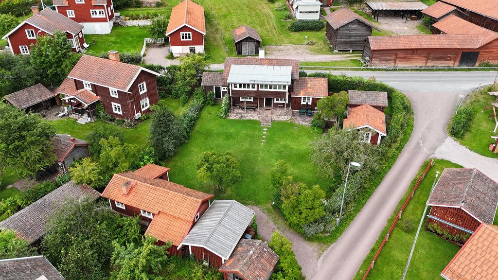 Översiktsbild över fastigheten som ligger på en hörntomt med generös trädgård, omgiven av charmiga byggnader i faluröd stil.