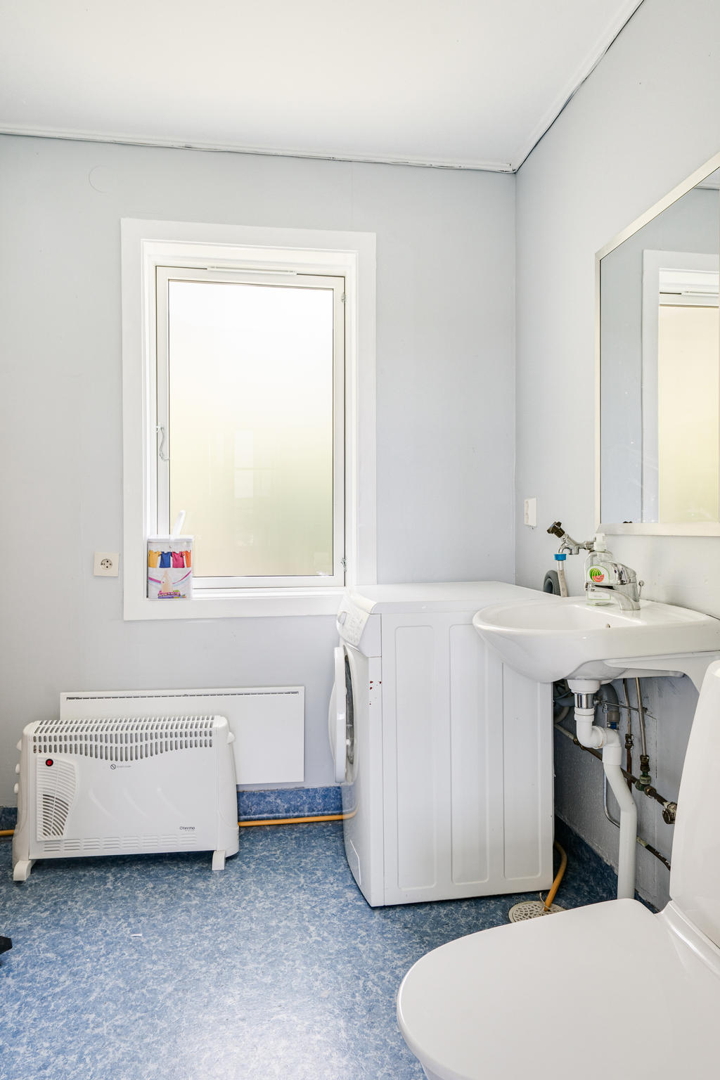 Tvättrum med toalett och tvättmaskin. 