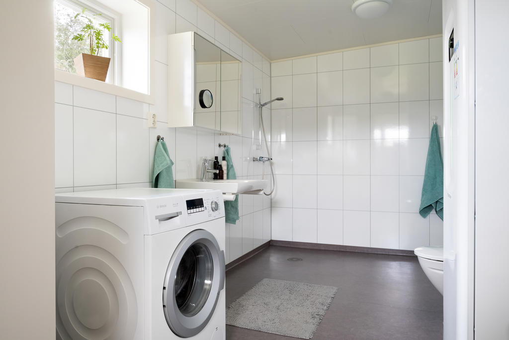 Det rymliga badrummet är smakfullt inrett och erbjuder en modern dusch, praktisk tvättmaskin samt stilrent handfat med spegel. Här kombineras funktionalitet med en fräsch och inbjudande tillvaro.