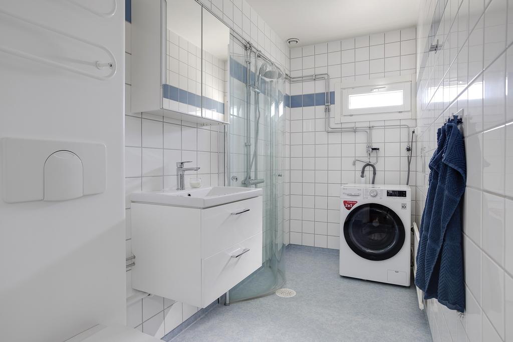 Halvkaklat badrum med kommod, spegelskåp, tvättmaskin och  dusch