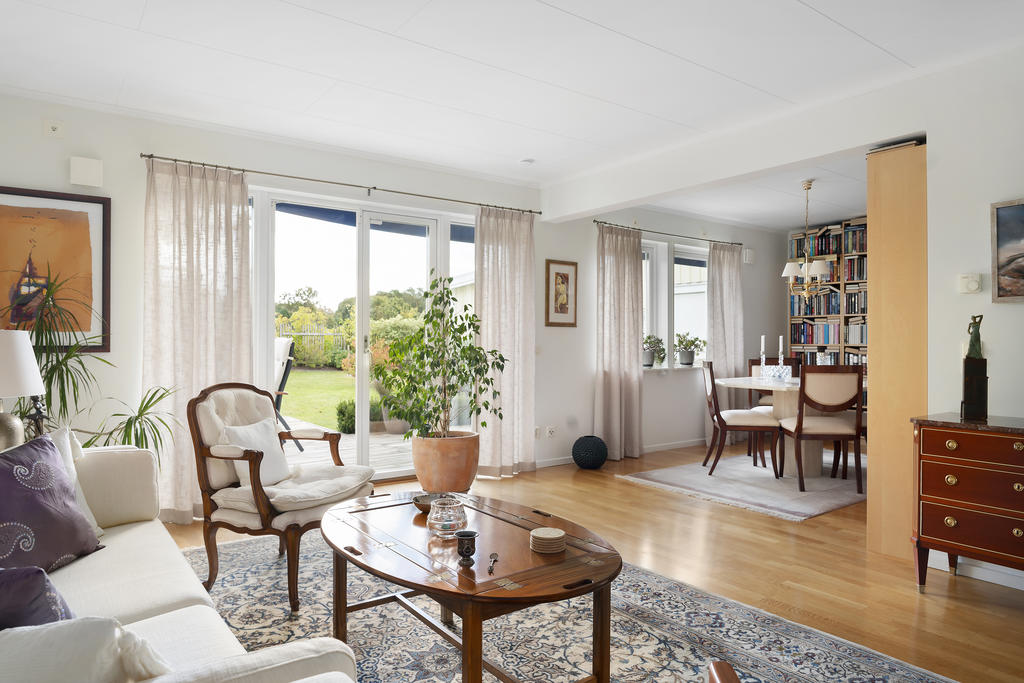 Trevligt vardagsrum med stora fönsterdörrar ut mot trädgård 