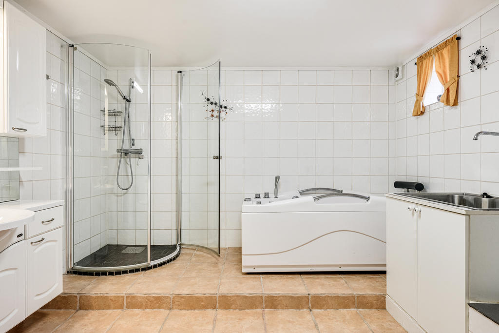 Rymligt badrum med duschkabin, badkar, tvättmaskin och el-golvvärme.