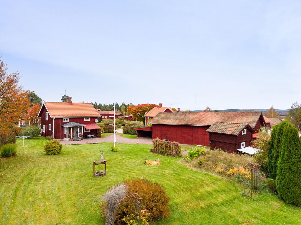 Charmig gård på hörntomt med vackra röda byggnader och en grönskande trädgård.