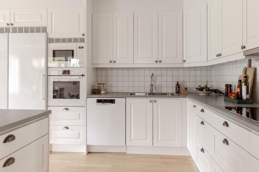 Köket är neutralt vitt med spegelluckor som kombineras snyggt tillsammans med vardagsrummets tidlösa spröjsade fönster 