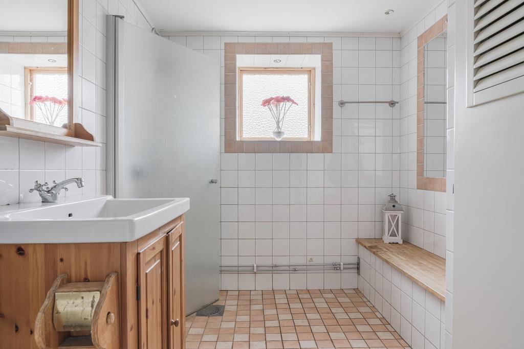 Helkaklat badrum på entréplan med dusch bakom frostat glas, fönster för ljusinsläpp och praktisk sittbänk.