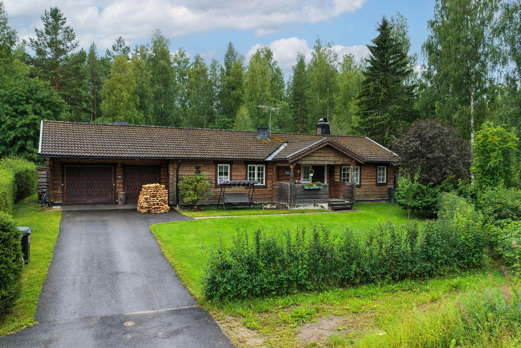 Fasad i norr med entré, asfalterad parkering samt ett vidbyggt garage. 
