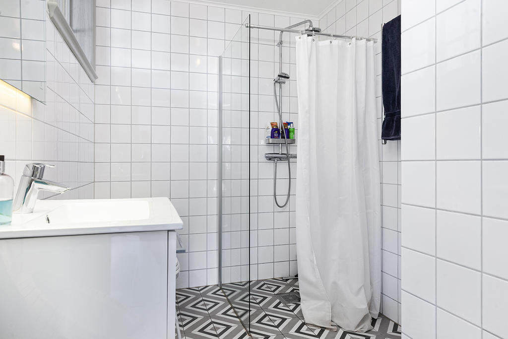Helkaklat badrum med dusch och tvättmaskin/torktumlare bakom pelaren till höger