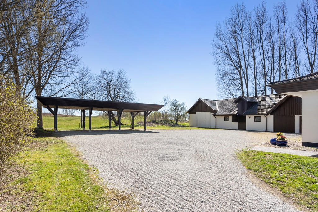 En stor gårdsplan med carport för tre bilar, garage, stall och traktorgarage till höger.