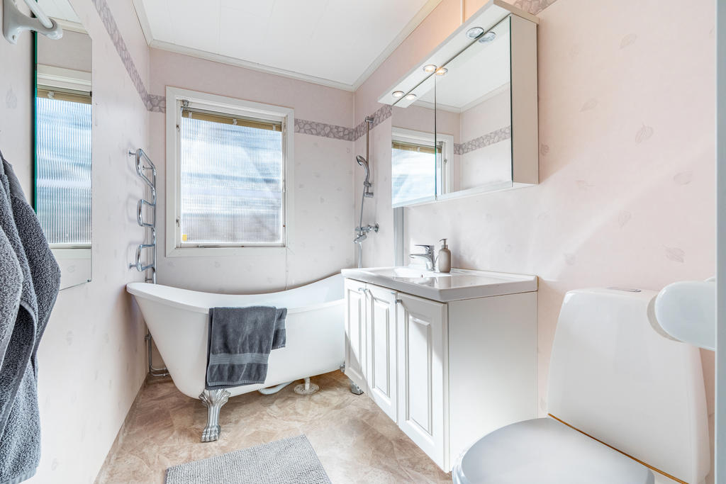 Fint och ljust badrum utrustat med wc, handfat med kommod, badrumsskåp, badkar och handdukstork.