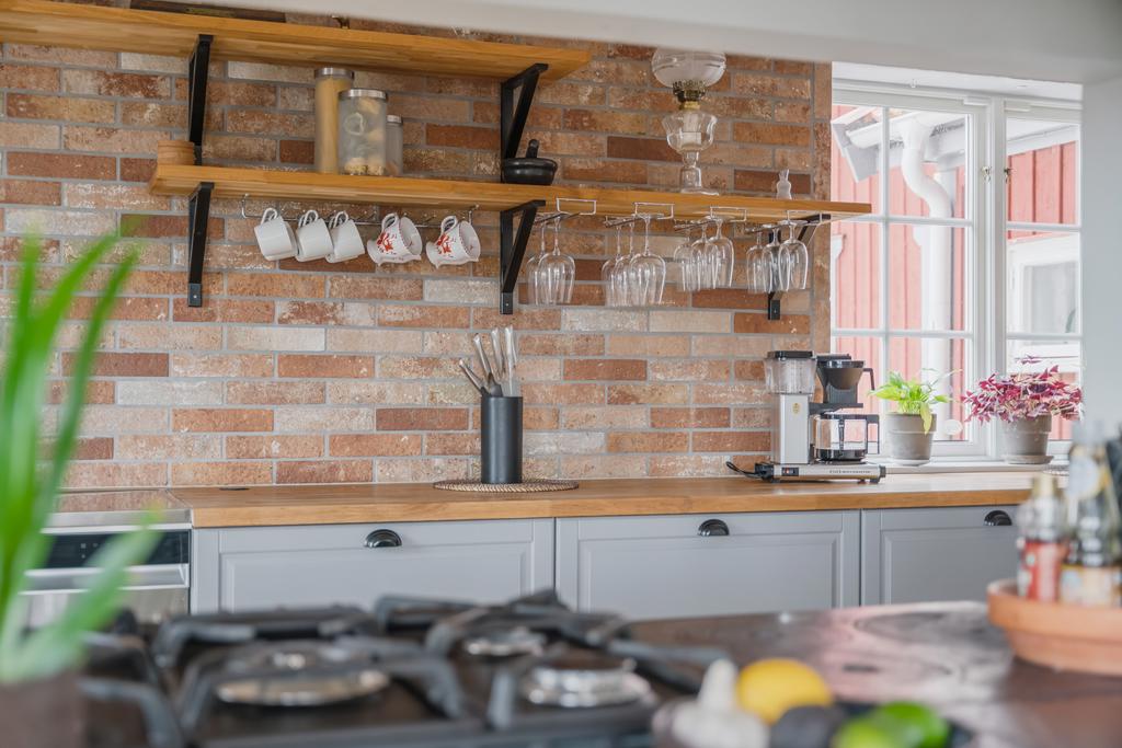 Detaljbild från kök med öppna hyllor, arbetsyta i trä samt tegelvägg som ger en varm och rustik karaktär.
