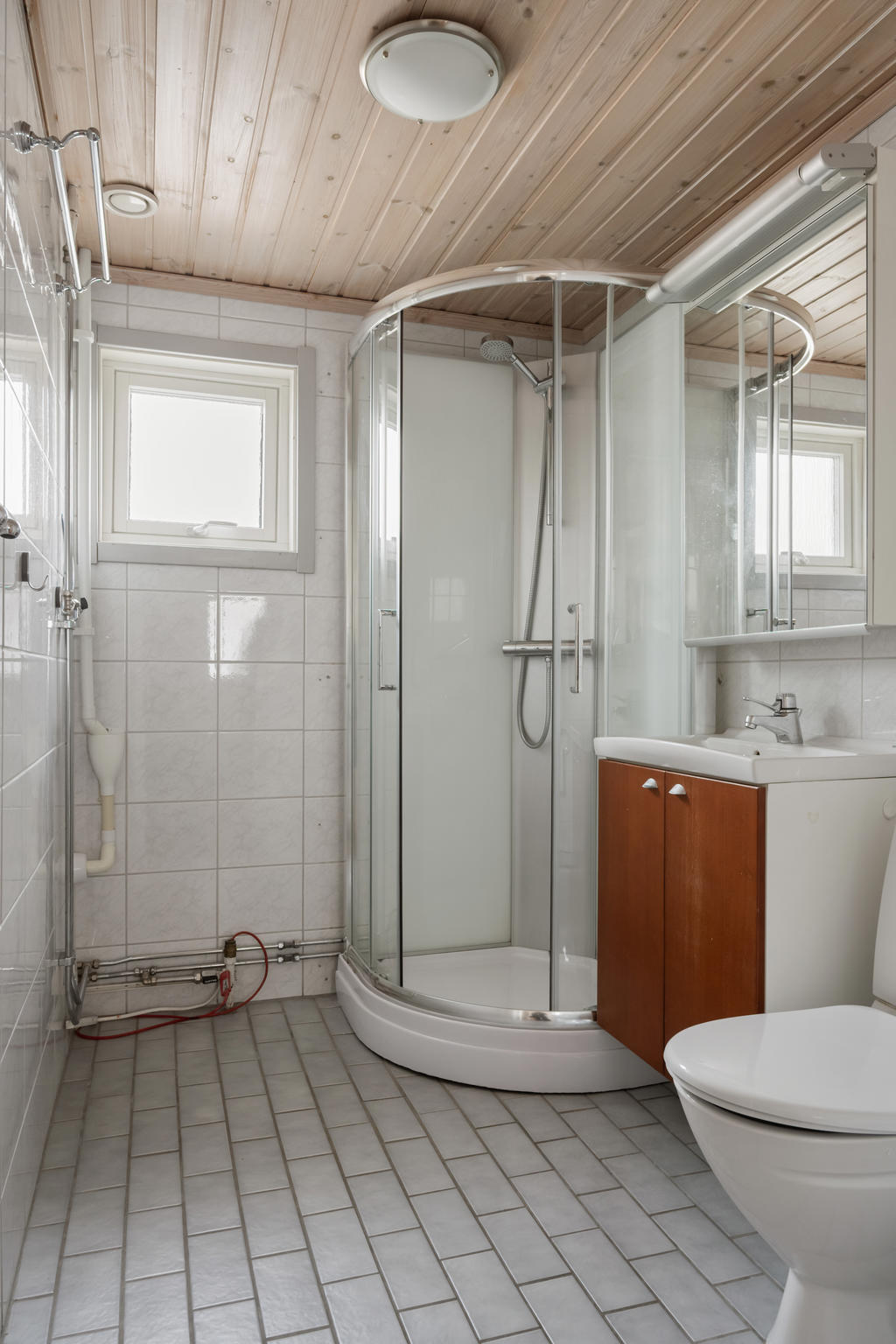 Helkaklat badrum med praktiska förvaringslösningar och en duschkabin. Här finns även en kommod med spegelskåp och wc för din bekvämlighet.