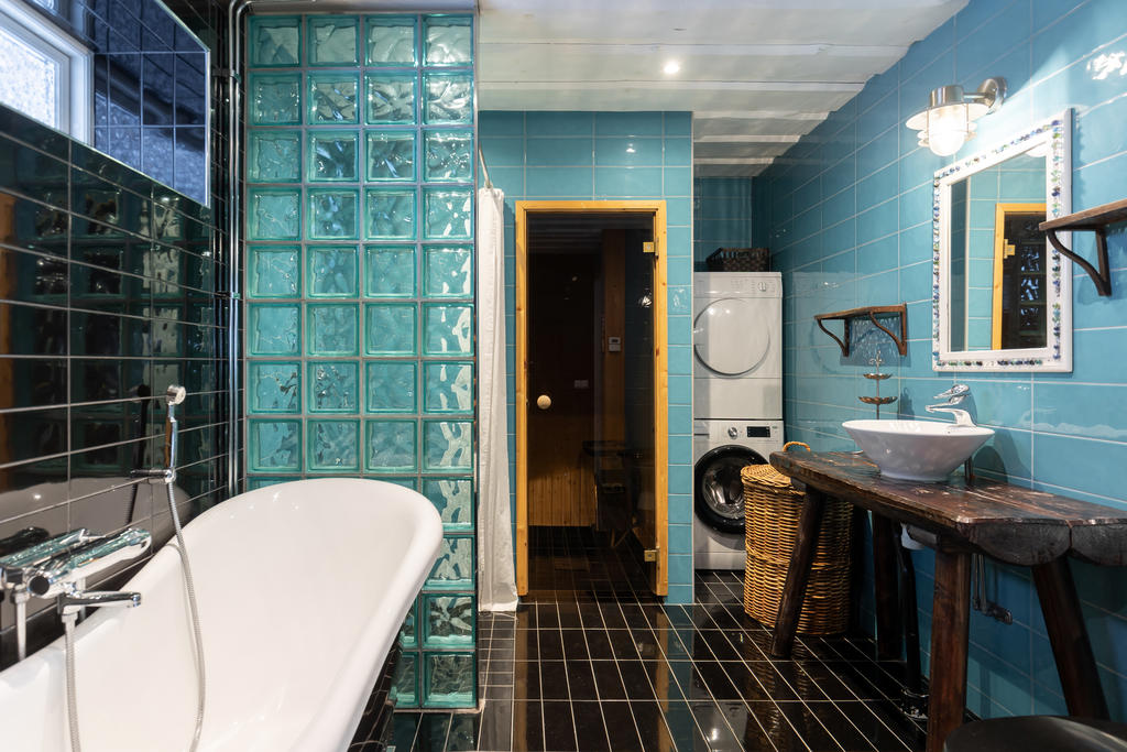 Rymligt badrum med badkar, dusch och bastu. Inrett med karaktäristiskt blått kakel, glasbetongväggar och svart klinkergolv.