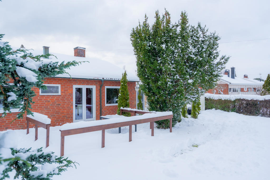 Baksidan med uteplats, gräsmatta och växtlighet. Bild taget i vackert snötäcke.