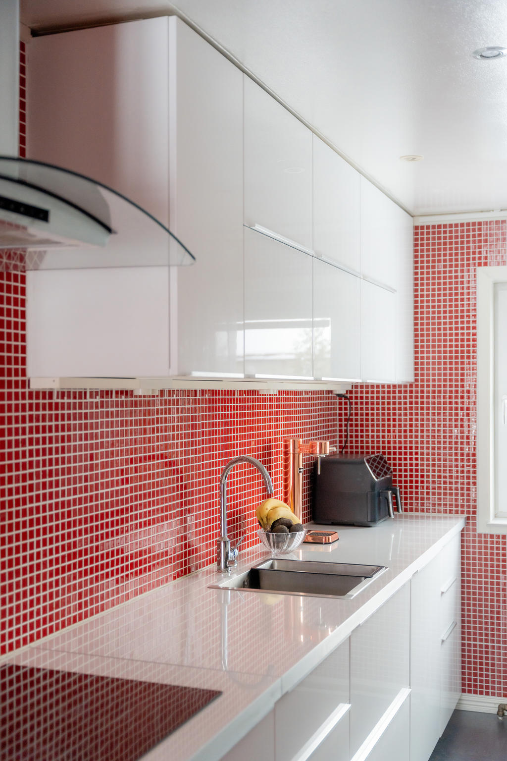 Detaljbild från köket. Rött mosaikkakel utgör en kontrast till den högblanka vita köksinredningen