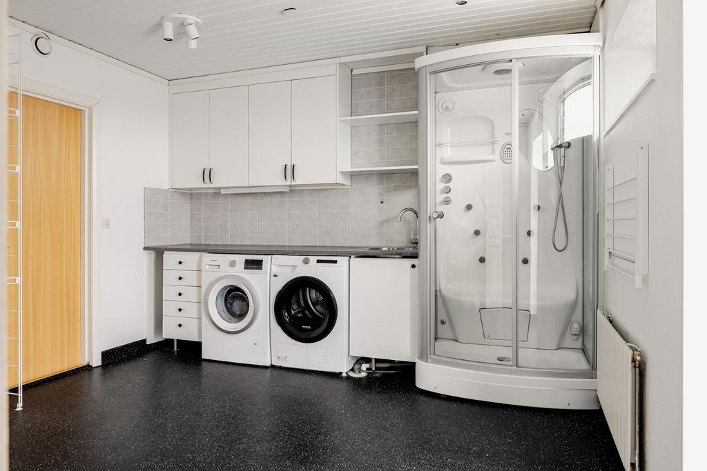 Tvättstuga med gott om förvaringsmöjligheter samt duschkabin. Innanför tvättstugan finns ett förråd. 