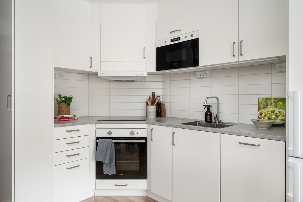 Effektivt planerat kök i vitt med laminatskiva och kaklat stänkskydd