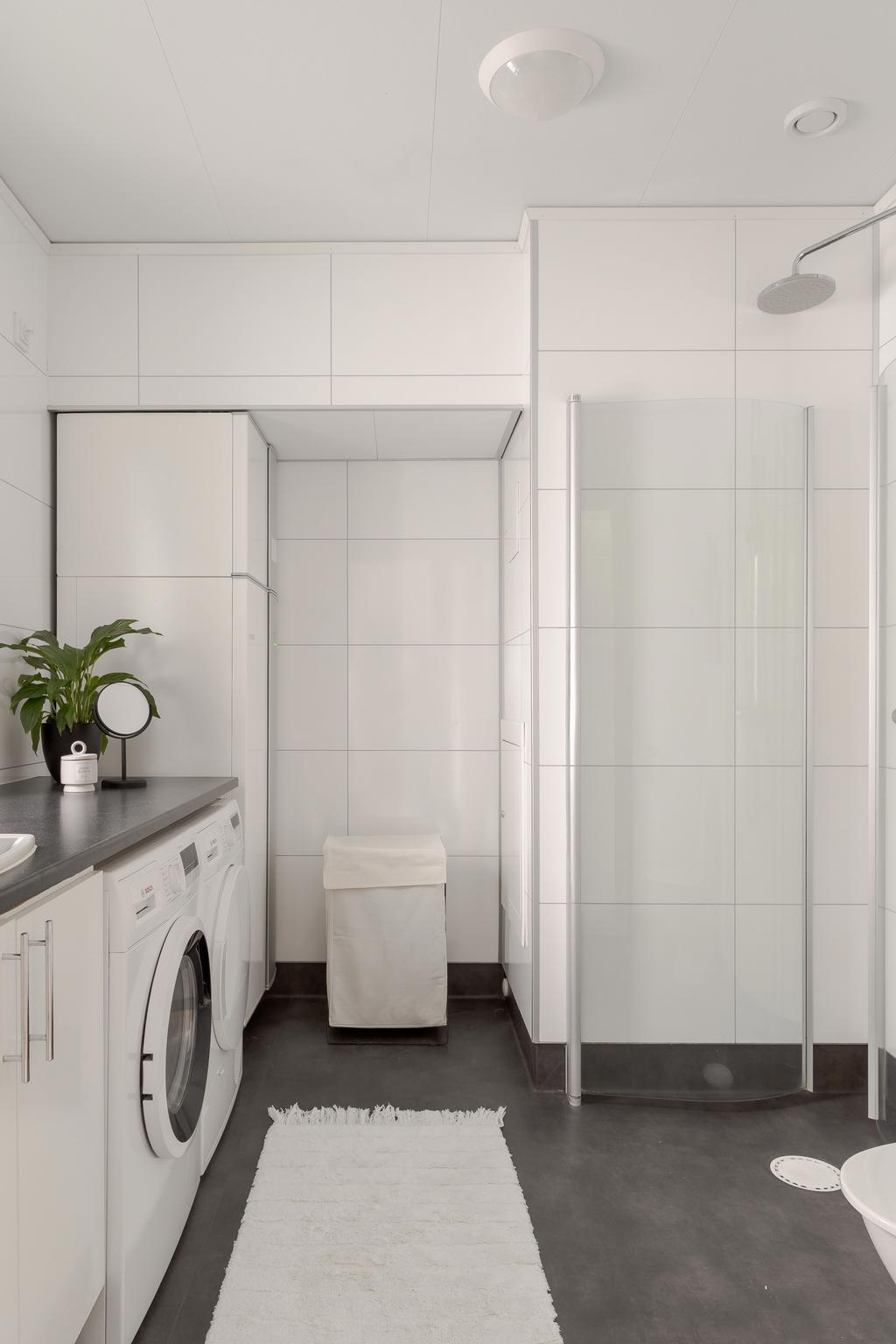 WC/Dusch med ljus inredning och arbetsyta ovan tvättmaskin och torktumlare.