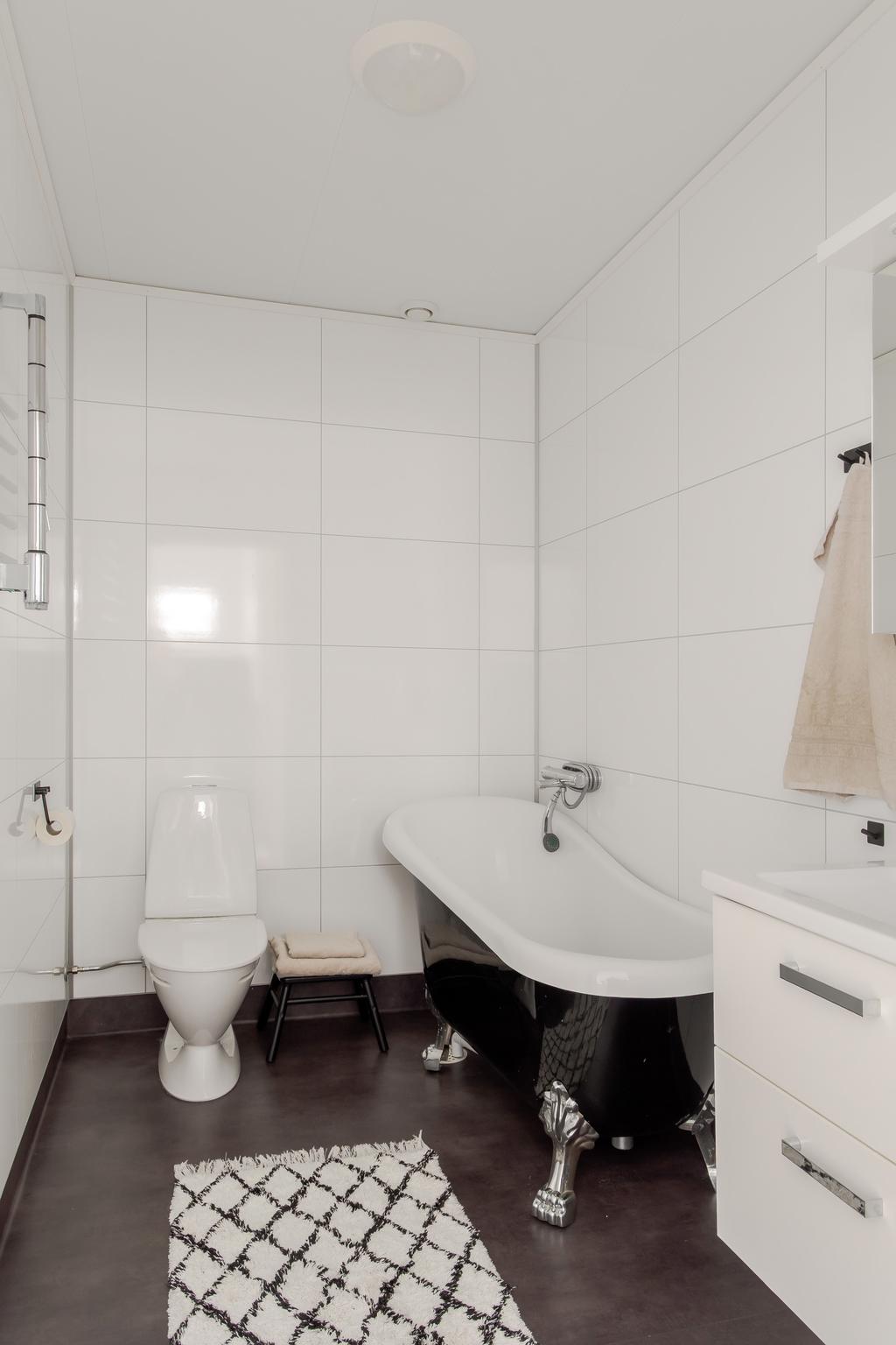 Ljust badrum på övre plan med våtrumsskivor på väggarna, plastmatta på golvet samt fristående badkar.