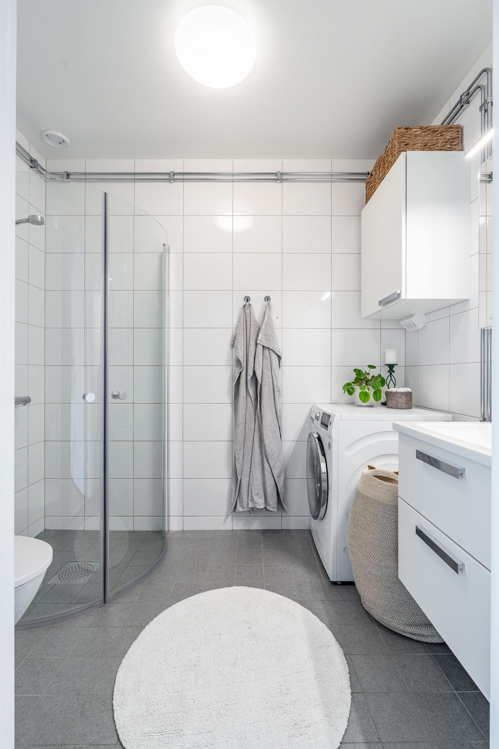 Stort helkaklat badrum utrustat med wc, handfat med kommod, dusch och tvättmaskin.