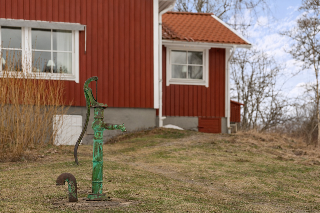 Pump med ingången till källaren i bakgrunden
 Bilden är årstidsredigerad