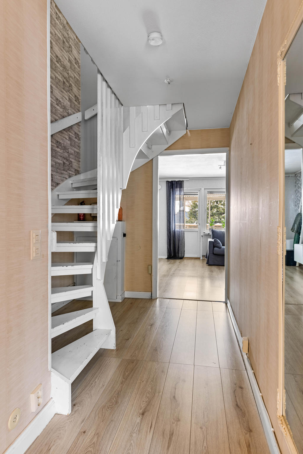 Hallkorridor med vy in till vardagsrum och trapp upp till övervåning. 
