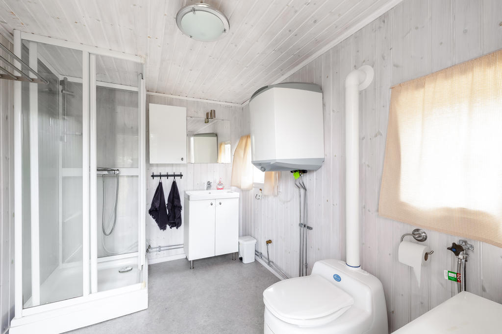 Badrum i separat byggnad med förbränningstoalett, handfat, duschkabin samt varmvattenberedare.