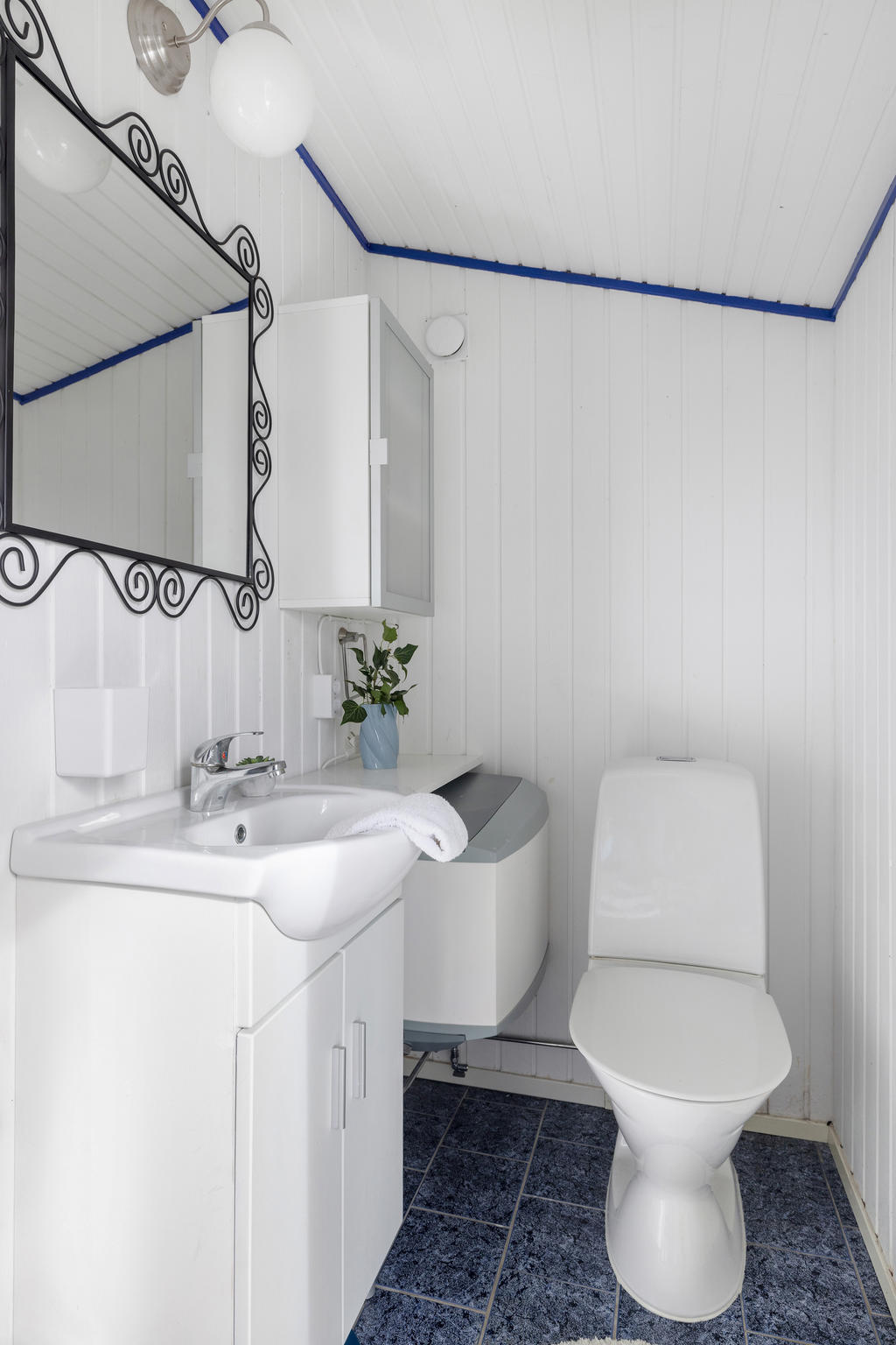 Mitt emot ligger toaletten. Här finns också handfat och varmvattensberedaren. Blått klinker och vit panelvägg