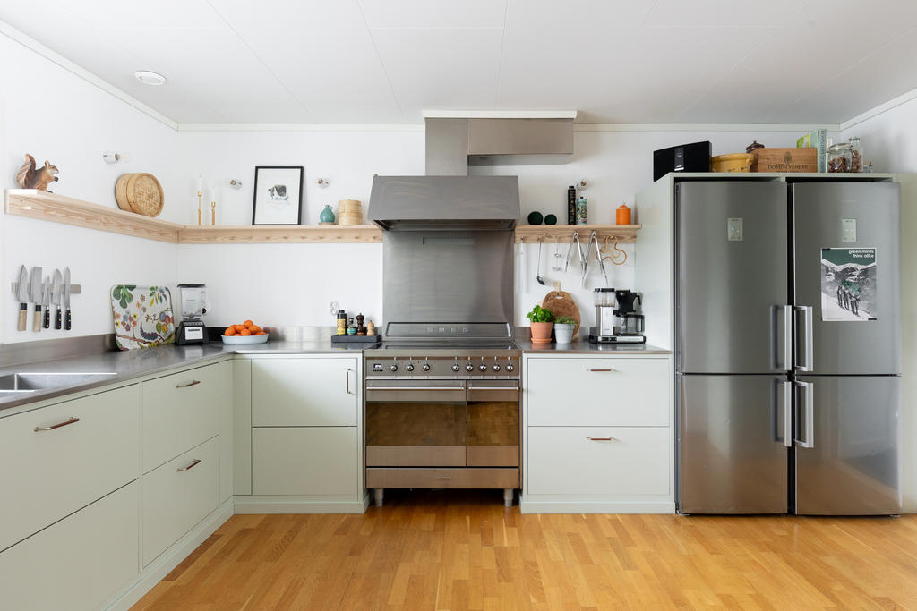 Smakfullt renoverat kök i en rogivande dovgrön nyans. De sobra luckorna bryts av med industriella inslag i rostfritt stål och en stor Smeg-spis/ugn. 