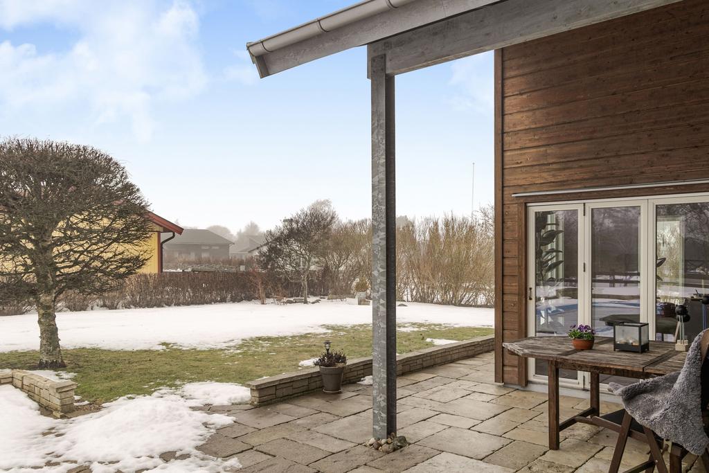 Stensatt uteplats med vardagsrummet innanför fönstren och poolen precis bredvid.