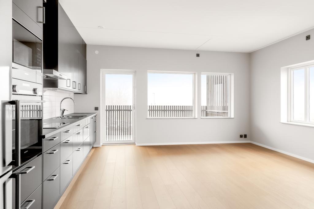 Ljust och öppet kök och vardagsrum i social planlösning med stora fönsterpartier och utgång till balkong.