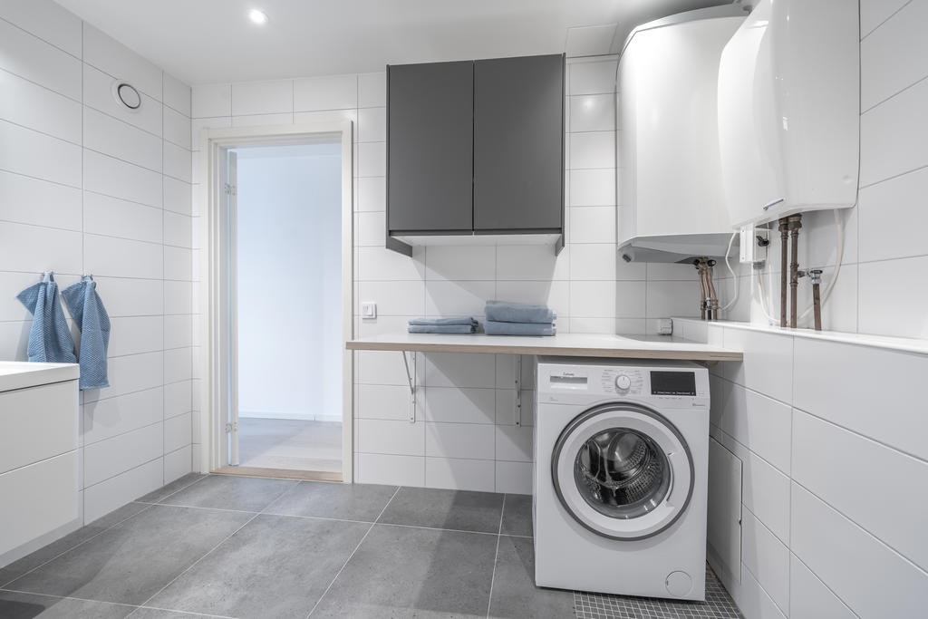 Tvättbänk med överskåp, tvättmaskin och varmvattenberedare.