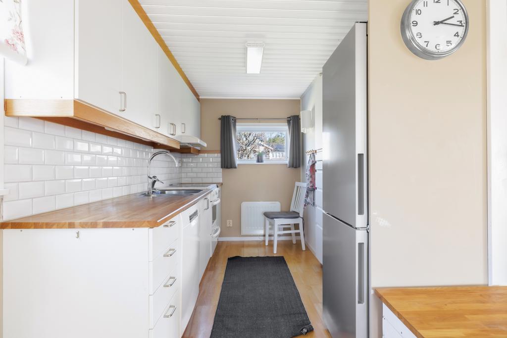 Ljust kök med vita skåp och luckor, vitt kakel över bänkskiva i massivt trä.