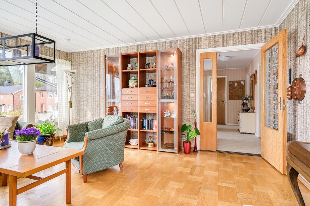 Hemtrevligt vardagsrum med stora glaspartier som ger mycket ljusinsläpp, fint parkettgolv samt utgång till trädgård.