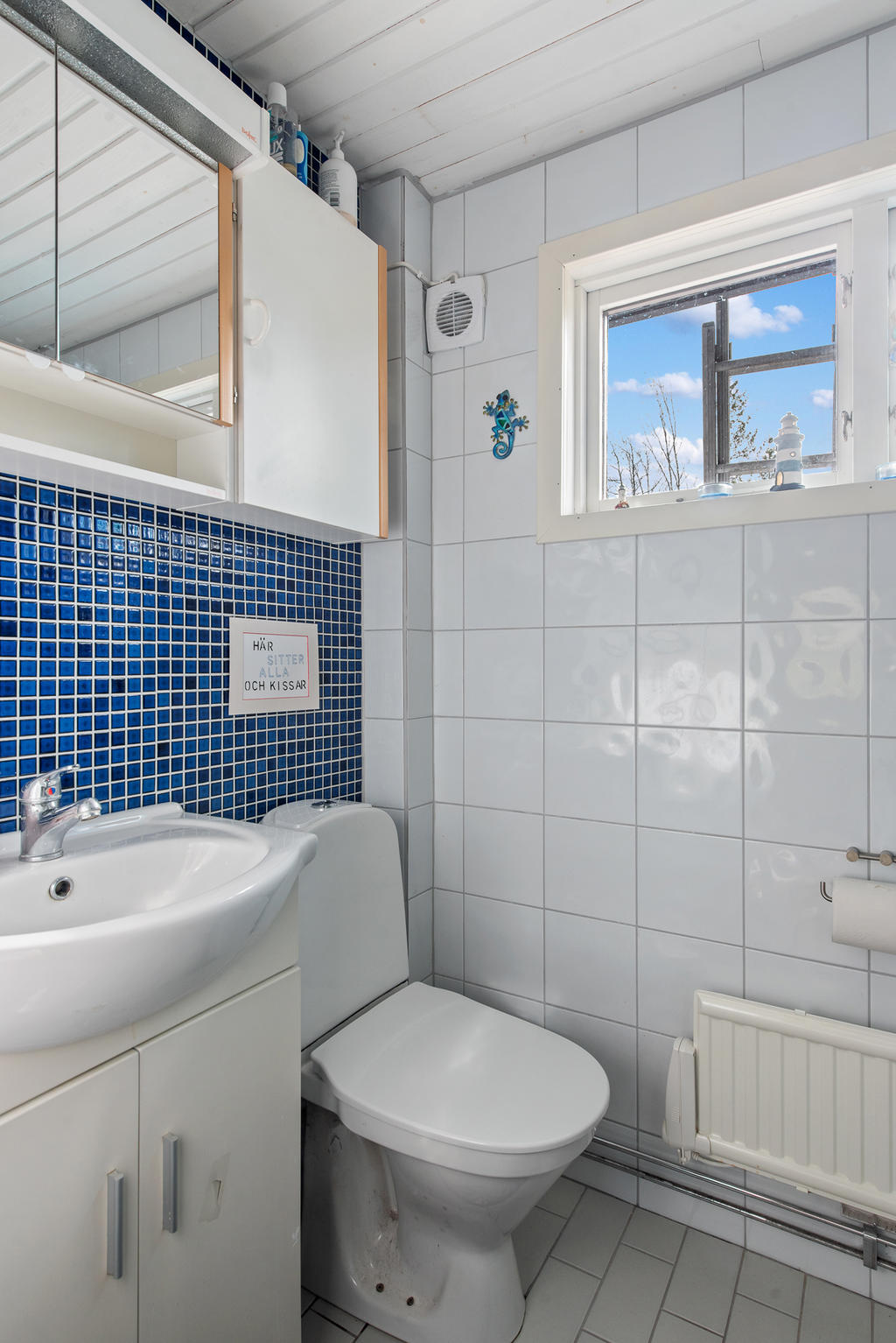 Wc, handfat, skåp och fönster i det helkaklade duschutrymmet