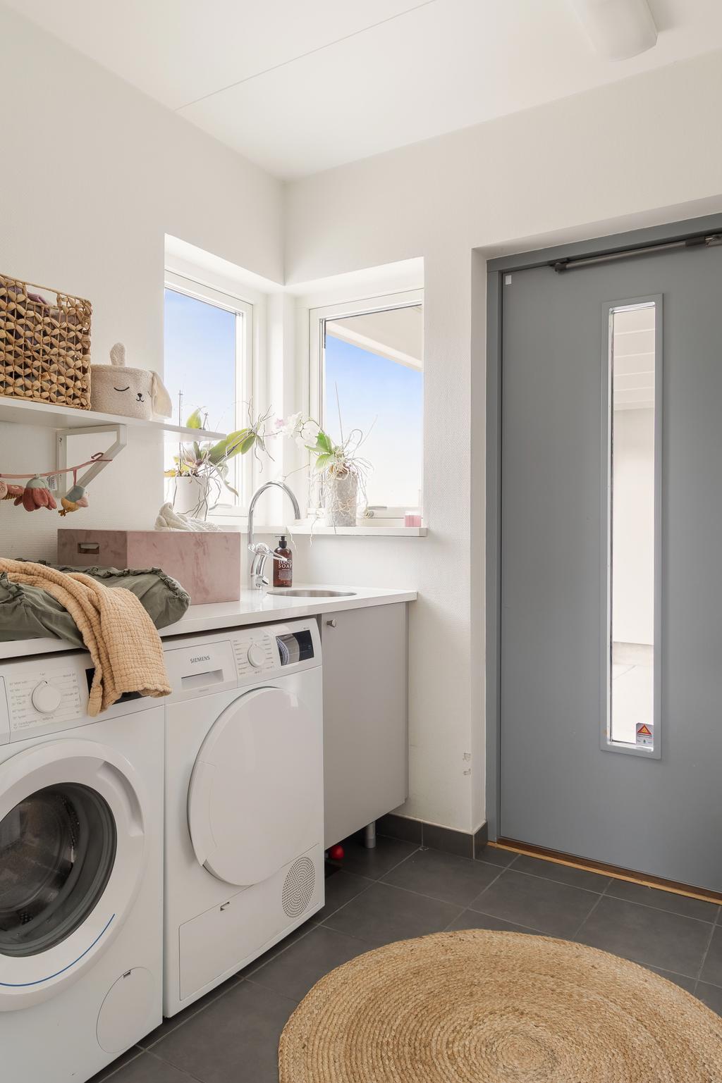 Praktisk tvättstuga med arbetsbänk, förvaring och fint ljusinsläpp, med entré mot carport.